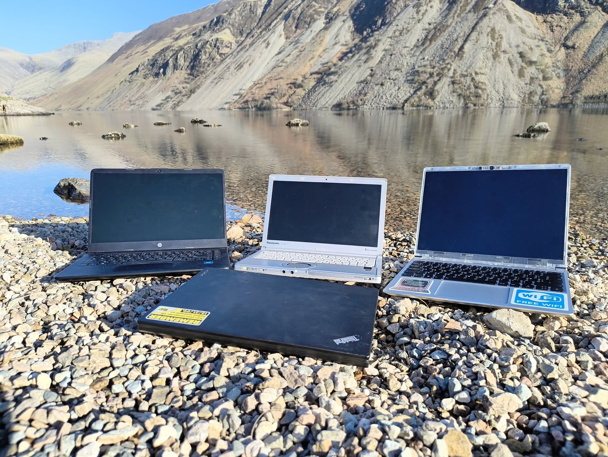 Three laptops displayed beside a mountain lake